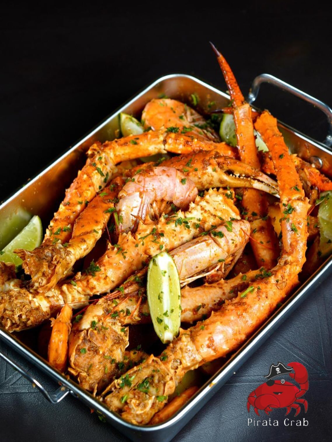 Pirata Crab steel tray of Cajun-sauced crab legs and prawns with lime wedges