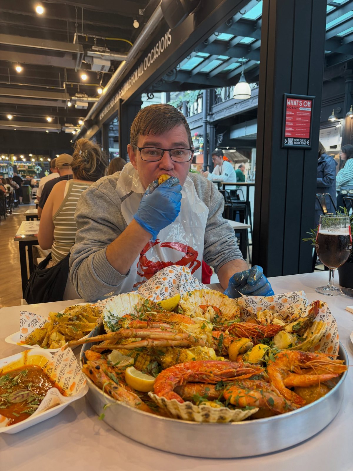 Diner with Deluxe Seafood Boil with extras (crab legs, prawns, corn) in food-hall setting